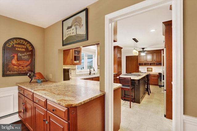 kitchen featuring stainless steel gas stovetop, sink, decorative light fixtures, light stone counters, and kitchen peninsula