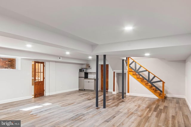 basement featuring stainless steel fridge and light hardwood / wood-style floors