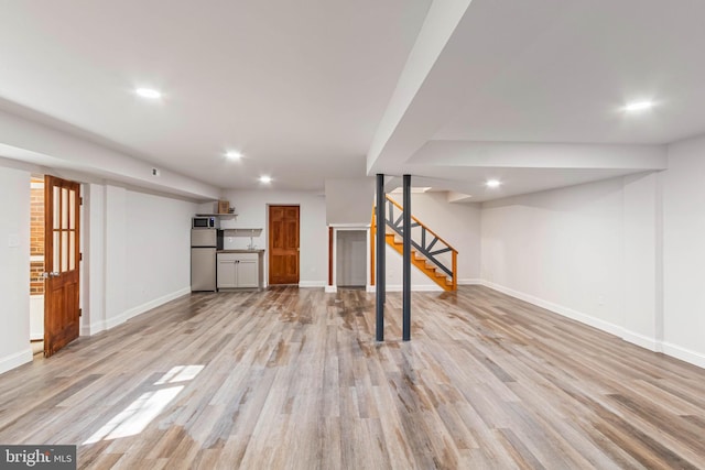 basement with stainless steel fridge and light wood-type flooring