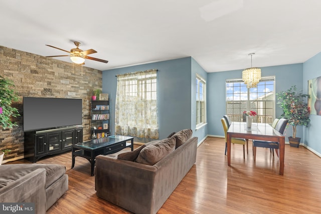 living room with ceiling fan with notable chandelier, light hardwood / wood-style flooring, and plenty of natural light