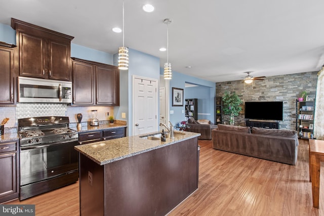 kitchen with sink, hanging light fixtures, black range with gas cooktop, an island with sink, and dark brown cabinets