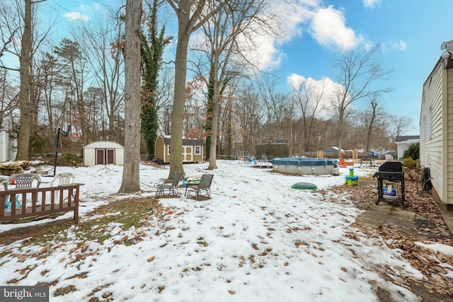 yard layered in snow featuring a shed, a trampoline, and a covered pool