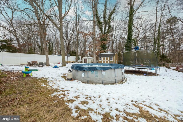 yard layered in snow featuring a covered pool, a storage shed, and a trampoline