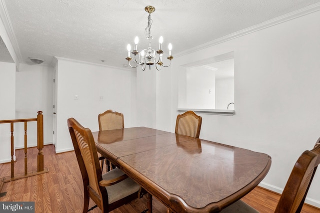 dining space with a textured ceiling, light wood-type flooring, crown molding, and an inviting chandelier