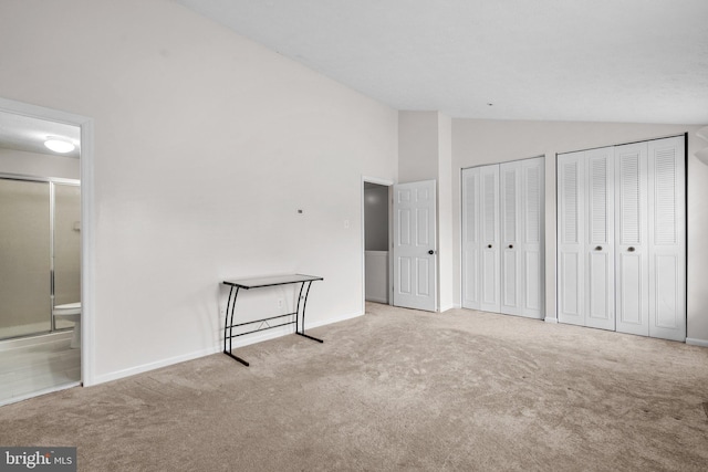 unfurnished bedroom with light colored carpet, multiple closets, high vaulted ceiling, and ensuite bath