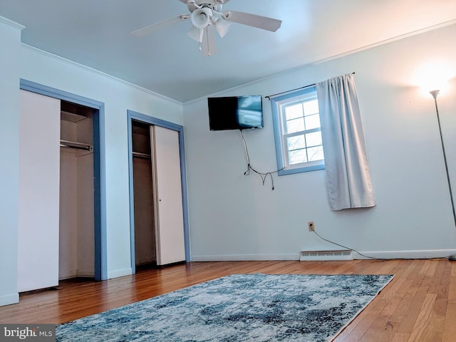 bedroom with ceiling fan, two closets, hardwood / wood-style floors, and crown molding