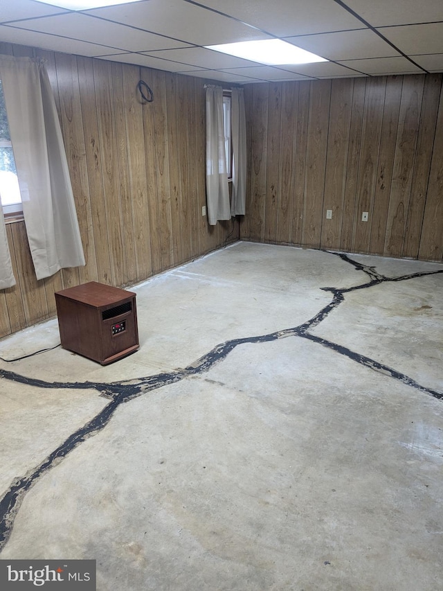 basement featuring a drop ceiling and wood walls