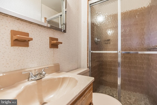 bathroom featuring a shower with door, vanity, and toilet