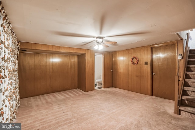 unfurnished bedroom featuring ensuite bath, wooden walls, a closet, and ceiling fan