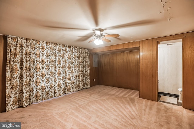 carpeted spare room with ceiling fan, electric panel, and wooden walls