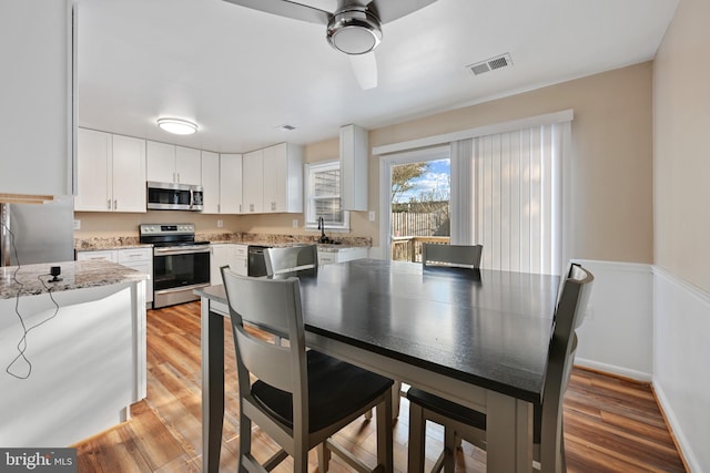 kitchen with light wood-type flooring, light stone counters, stainless steel appliances, ceiling fan, and white cabinets