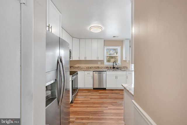 kitchen featuring appliances with stainless steel finishes, light wood-type flooring, light stone counters, sink, and white cabinetry