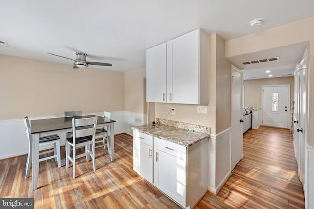 kitchen featuring white cabinets, ceiling fan, light hardwood / wood-style floors, and light stone counters