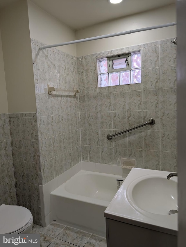 full bathroom featuring vanity, tile patterned floors, tiled shower / bath combo, toilet, and tile walls