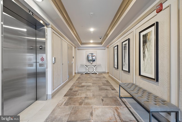 hallway featuring ornamental molding, a raised ceiling, and elevator