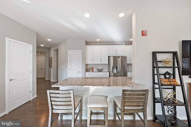 kitchen with stainless steel fridge, white cabinetry, backsplash, a kitchen breakfast bar, and light stone counters