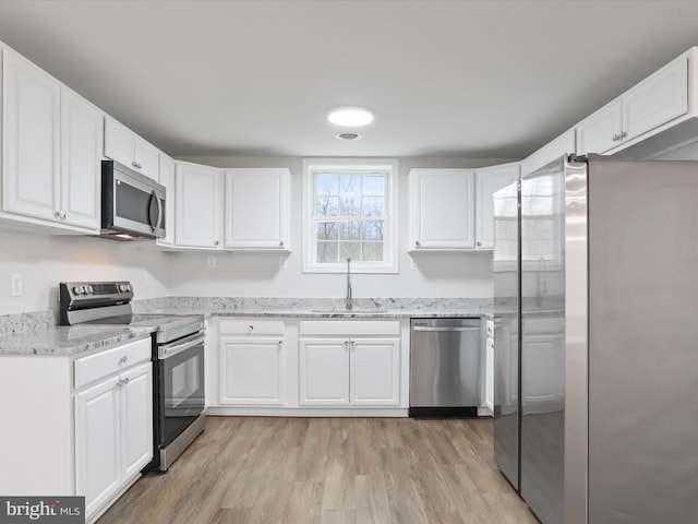 kitchen featuring white cabinets, appliances with stainless steel finishes, light stone counters, and sink