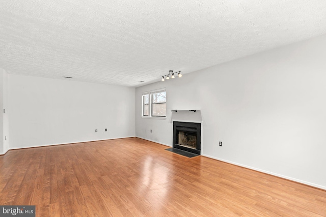 unfurnished living room with light wood-type flooring, a textured ceiling, and rail lighting