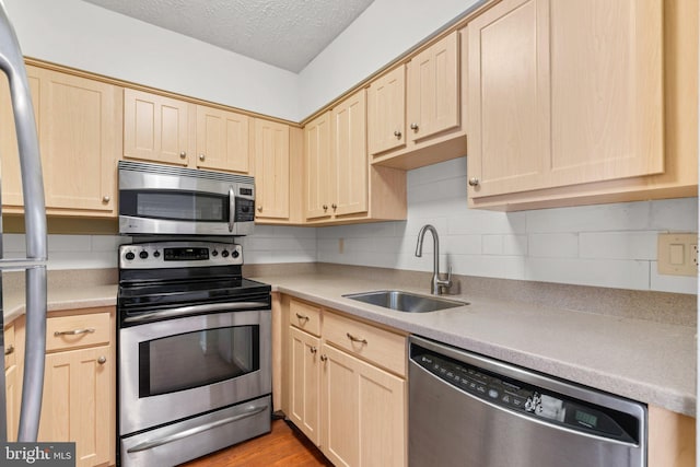 kitchen featuring appliances with stainless steel finishes, tasteful backsplash, light brown cabinetry, sink, and light wood-type flooring