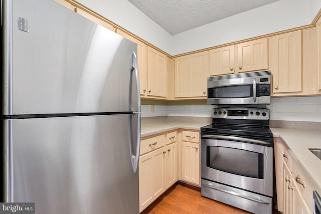 kitchen featuring stainless steel appliances, light brown cabinets, tasteful backsplash, light wood-type flooring, and a textured ceiling