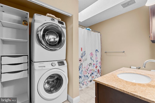 clothes washing area featuring sink, light tile patterned floors, and stacked washer and clothes dryer