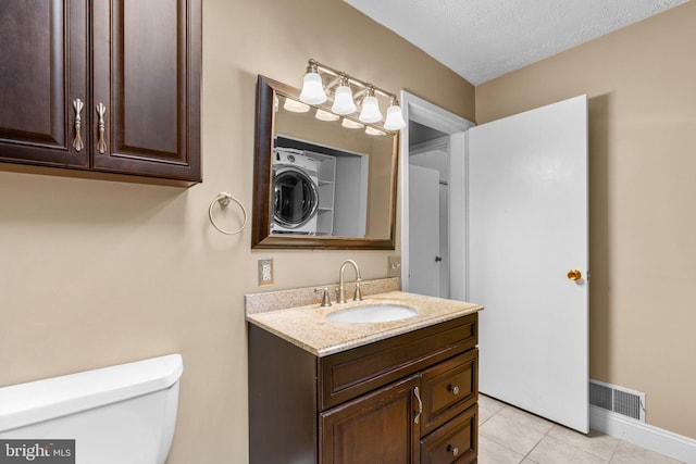 bathroom featuring a textured ceiling, tile patterned flooring, vanity, toilet, and stacked washing maching and dryer