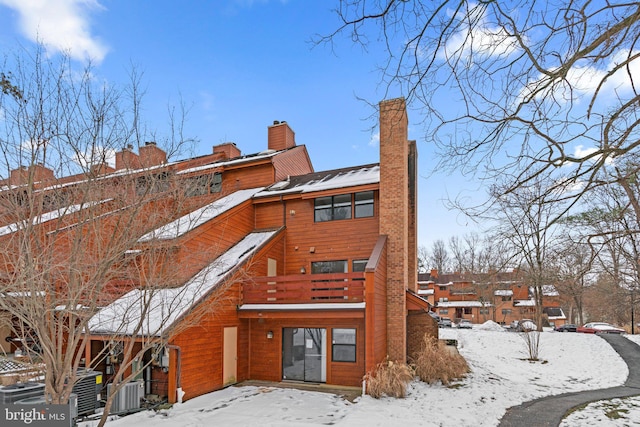 snow covered rear of property with central AC unit and a balcony