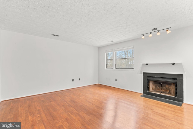 unfurnished living room with a textured ceiling, track lighting, and light wood-type flooring