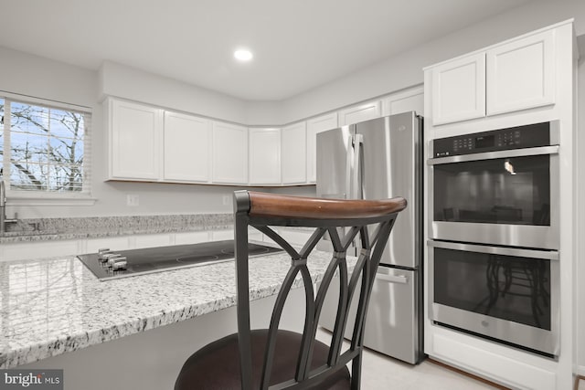 kitchen with white cabinets, light stone countertops, stainless steel appliances, and a breakfast bar area