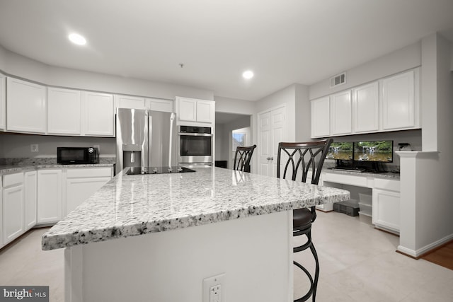 kitchen with light stone countertops, a kitchen island, a breakfast bar, white cabinets, and black appliances