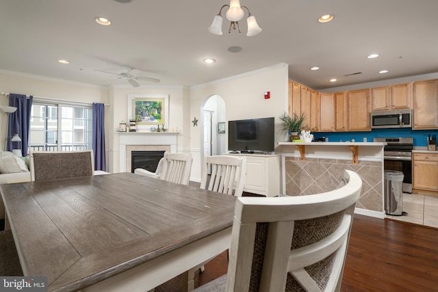 dining room featuring a tiled fireplace, ceiling fan, dark hardwood / wood-style flooring, and ornamental molding