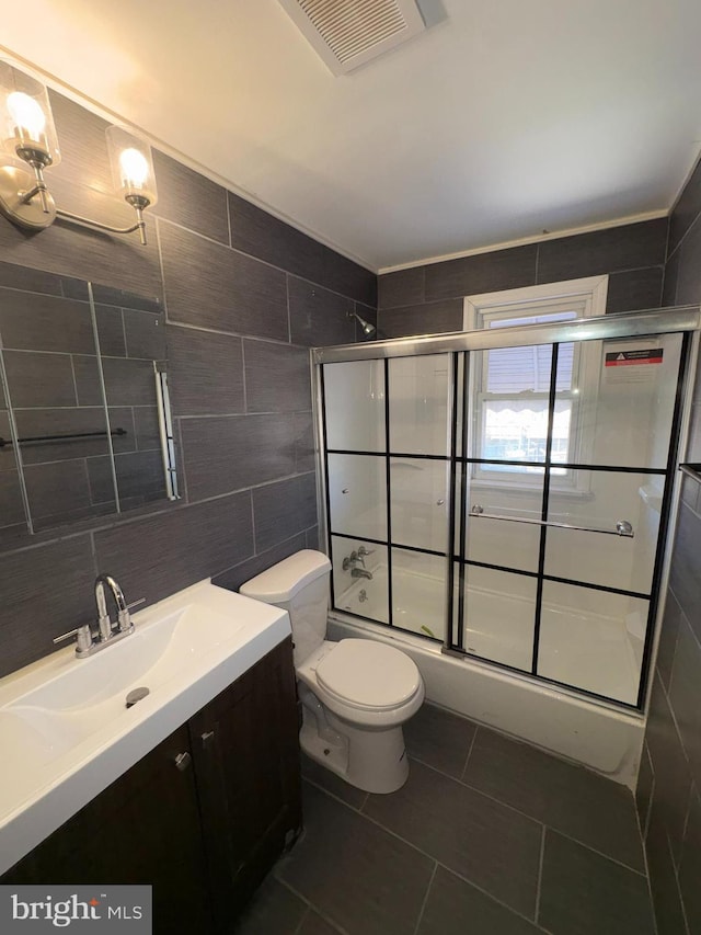 full bathroom with tile patterned flooring, combined bath / shower with glass door, toilet, vanity, and tile walls