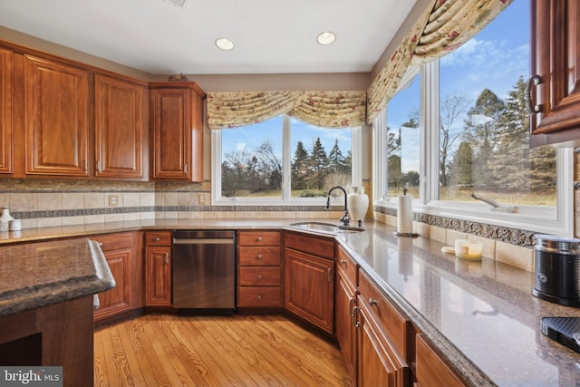 kitchen featuring decorative backsplash, light wood-type flooring, dishwasher, light stone countertops, and sink