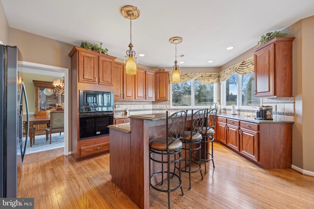 kitchen featuring decorative light fixtures, a kitchen breakfast bar, a kitchen island, light hardwood / wood-style flooring, and black appliances