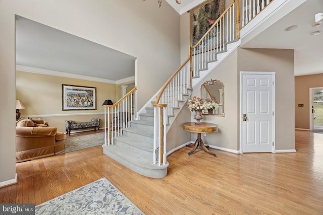 stairway featuring a towering ceiling, ornamental molding, and hardwood / wood-style flooring