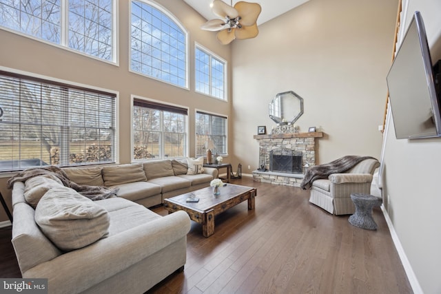 living room featuring ceiling fan, dark hardwood / wood-style flooring, a high ceiling, and a stone fireplace