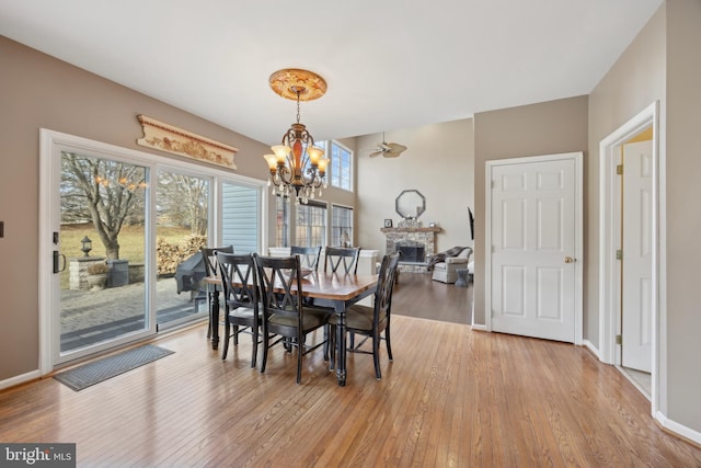 dining area featuring wood-type flooring, a notable chandelier, and a stone fireplace