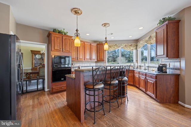 kitchen featuring tasteful backsplash, light wood-type flooring, a kitchen island, a breakfast bar, and black appliances