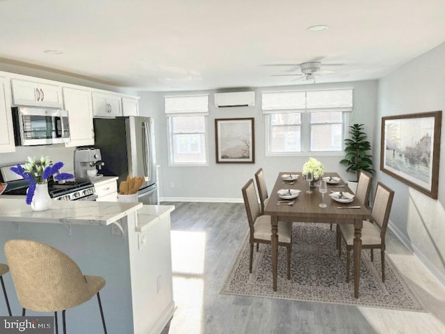 kitchen with a kitchen bar, a wall mounted air conditioner, stainless steel appliances, hardwood / wood-style flooring, and white cabinets