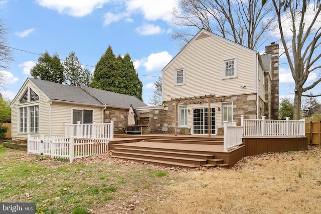 back of property featuring a pergola, a deck, stone siding, and a chimney