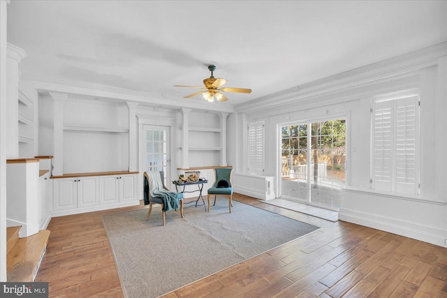 living area with ceiling fan, light wood-type flooring, built in features, and ornamental molding