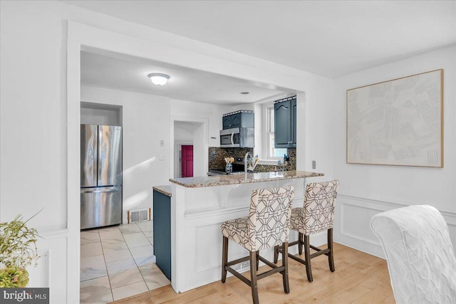 kitchen with a breakfast bar, light stone countertops, blue cabinetry, kitchen peninsula, and stainless steel appliances