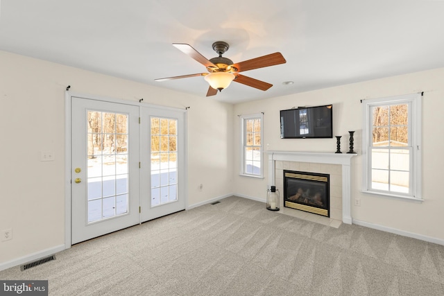 unfurnished living room with a tile fireplace, a wealth of natural light, light colored carpet, and ceiling fan