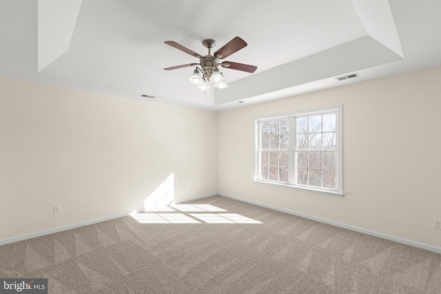 empty room featuring ceiling fan, light carpet, and a tray ceiling