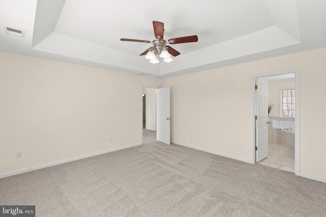 unfurnished bedroom featuring ensuite bath, light carpet, and a tray ceiling