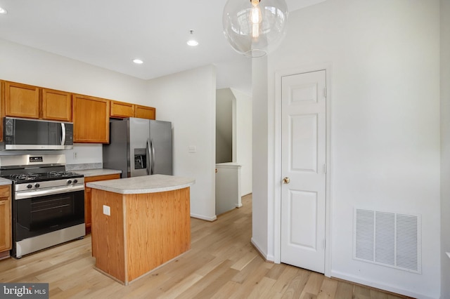 kitchen with decorative light fixtures, a center island, appliances with stainless steel finishes, and light hardwood / wood-style flooring