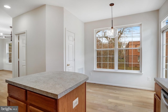 kitchen featuring stainless steel dishwasher, decorative light fixtures, an inviting chandelier, light hardwood / wood-style flooring, and a kitchen island