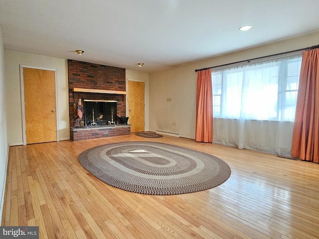 unfurnished living room with light hardwood / wood-style floors, a brick fireplace, and a baseboard heating unit