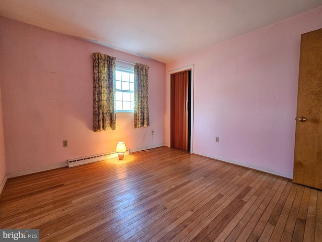 unfurnished room featuring baseboard heating and light hardwood / wood-style floors