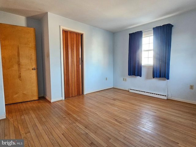 unfurnished room with light wood-type flooring and a baseboard heating unit